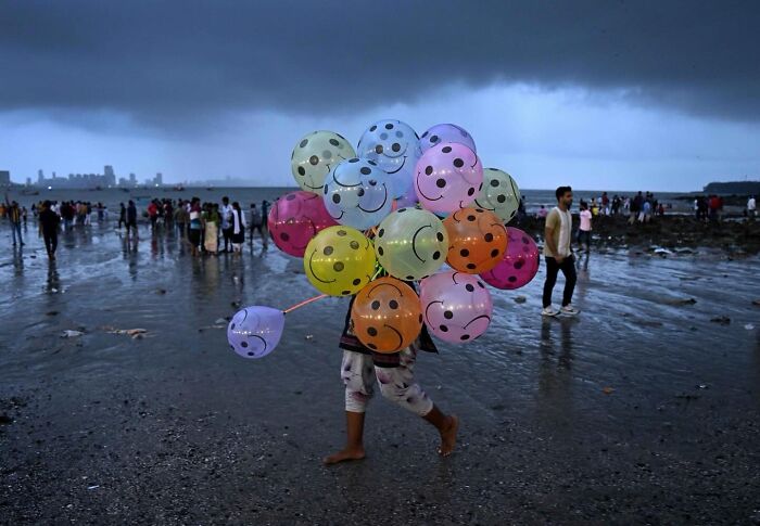 Child selling colorful smiley face balloons on a crowded Mumbai street during a cloudy evening, capturing everyday life.