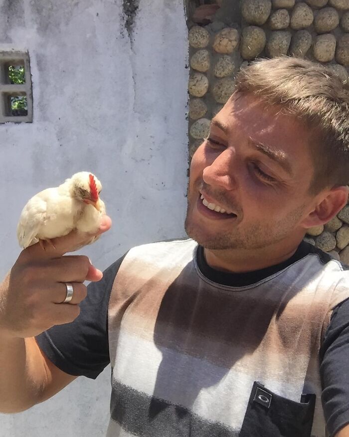 Man smiling while holding a small bird, showing a close bond with a wild vulture in an outdoor setting. Man smiling while holding a small bird, showing a close bond with a wild vulture in an outdoor setting.