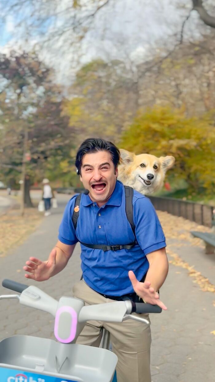 Man laughing while riding bike with dog in backpack on city path during autumn city adventures