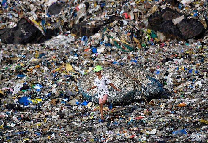 Child wearing a green cap walking through a large pile of trash in a street photo capturing everyday life in Mumbai.