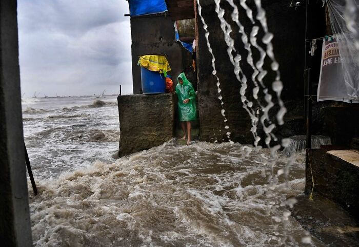 Person wearing green raincoat stands near flooded street during heavy rain in Mumbai capturing everyday life.