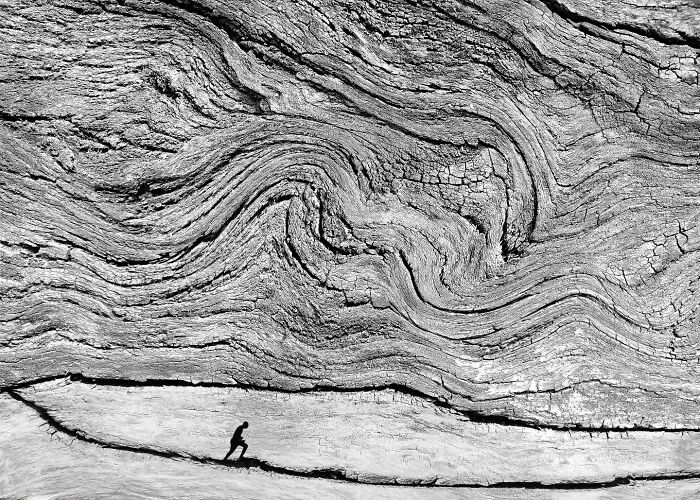 Minimalist black and white photograph showing a small running figure contrasted against textured, swirling wood patterns by a striking photographer.