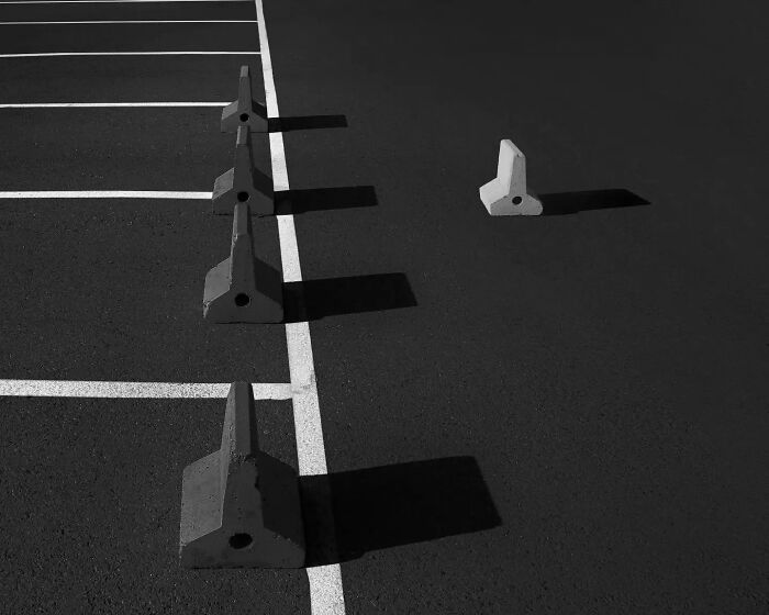 Minimalist black and white photo of concrete parking blocks casting long shadows on asphalt, showcasing artful minimalism photography.