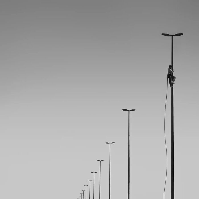 Minimalist black and white photo of a person climbing a tall streetlight, showcasing striking minimalism in photography art.