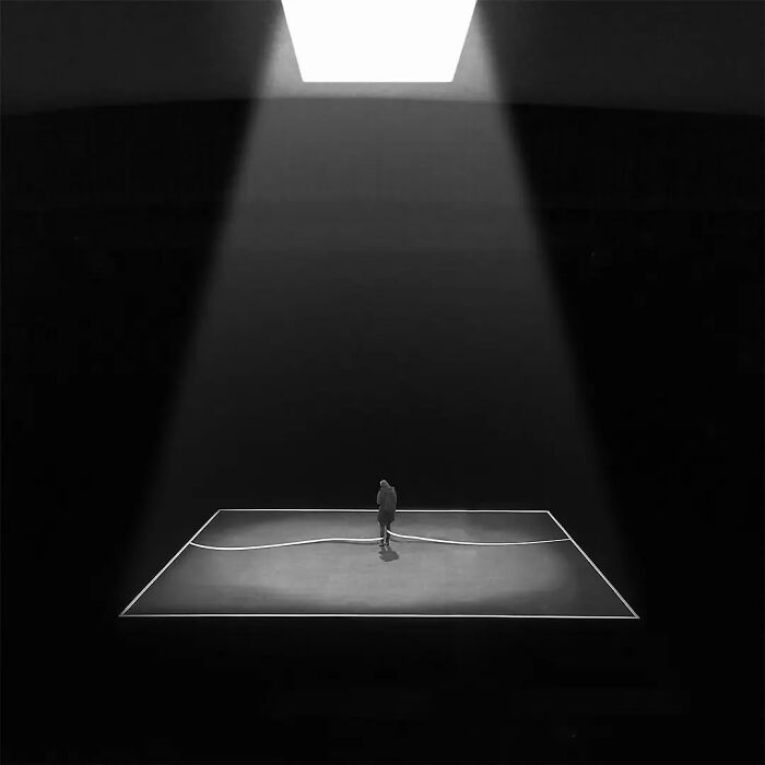 Minimalism art photo showing a solitary figure illuminated by a single overhead light in a dark, empty space.