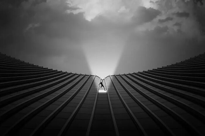 Silhouette of a person standing between curved building lines with sun rays in a minimalist architectural image.