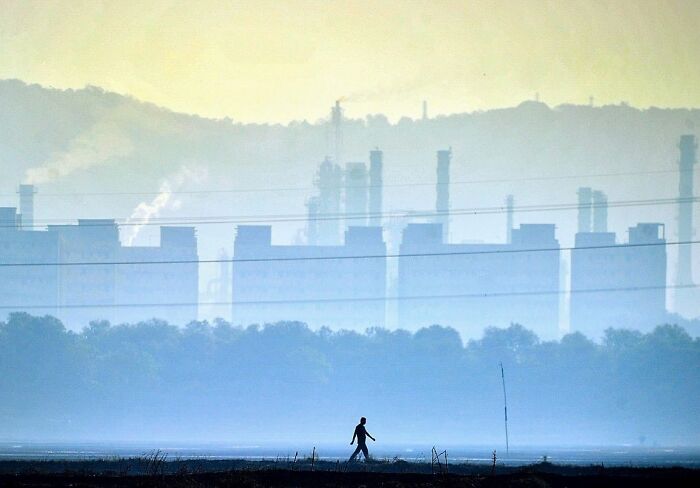 Silhouetted person walking with industrial buildings and hazy skyline in a stunning street photo of everyday life in Mumbai.
