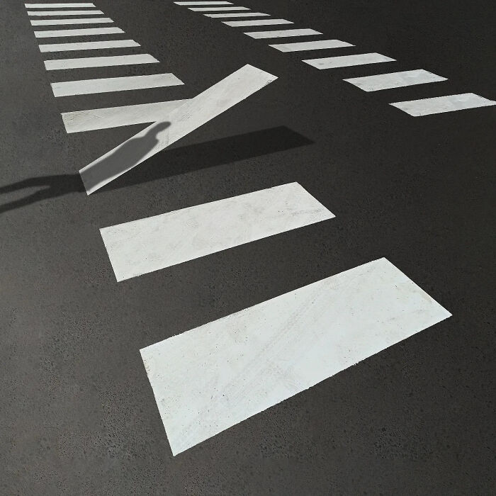Minimalism in art shown by a photographer with a shadow lifting a painted white street line on dark asphalt.