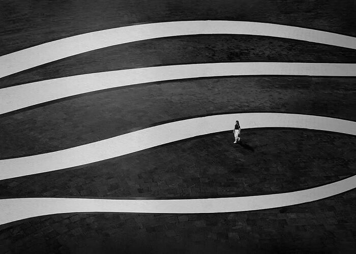 Person walking on a curved path in a minimalist black and white composition showcasing striking photography art.