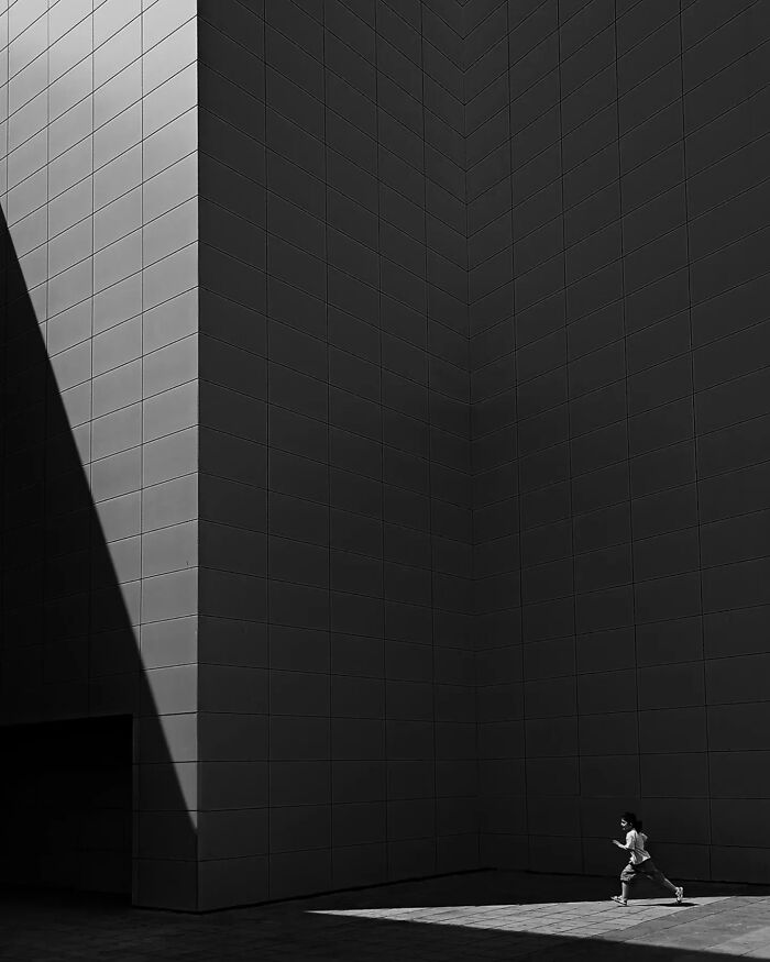 Minimalism art black and white image of large geometric building with sunlight and a child running in the corner.