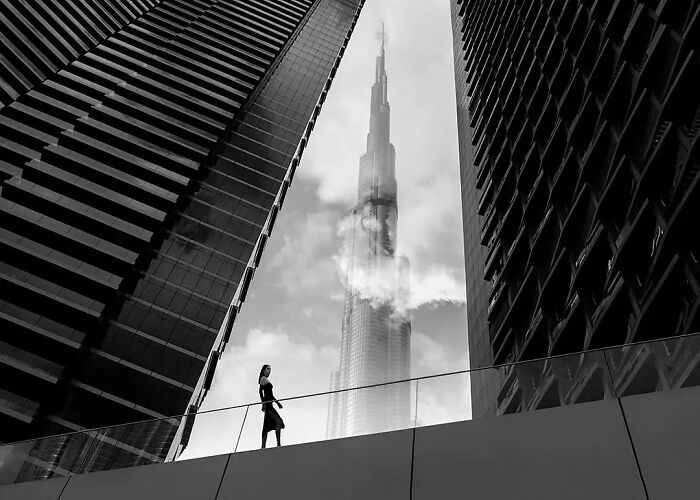 Minimalism art in photography showcasing a lone figure between towering modern buildings with a misty skyscraper backdrop.