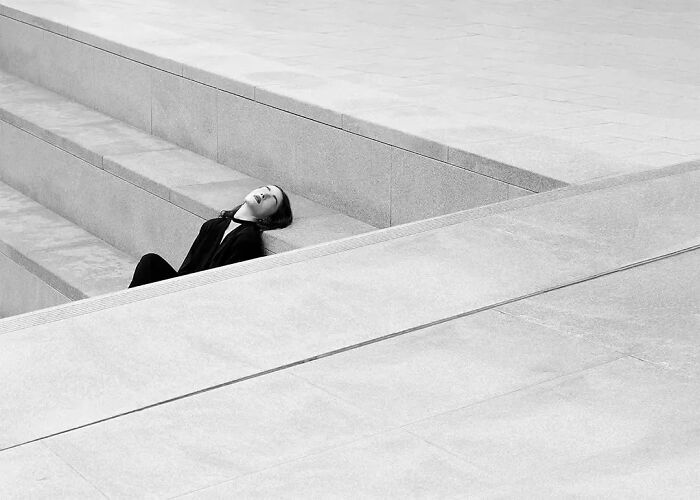 Woman in black clothing resting on concrete steps in a minimalism-inspired striking image by a photographer using art techniques