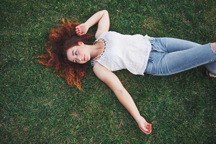 Woman with curly red hair lying on grass, showcasing fascinating human body features and facts in a natural setting