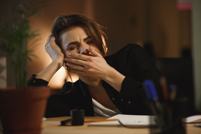 Woman covering mouth yawning tiredly at desk, illustrating fascinating human body features and facts.