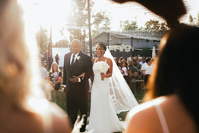 Bride walking down the aisle with father at outdoor wedding ceremony, capturing couple split at altar moment.