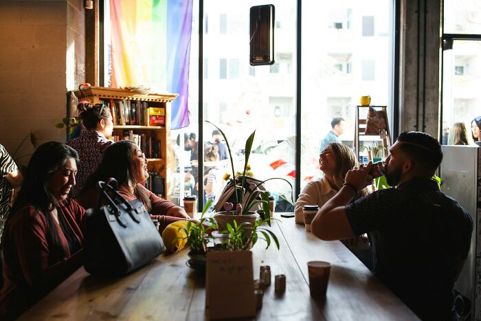 Group of friends talking and laughing at a cafe, highlighting harmless but toxic habits in a social setting.