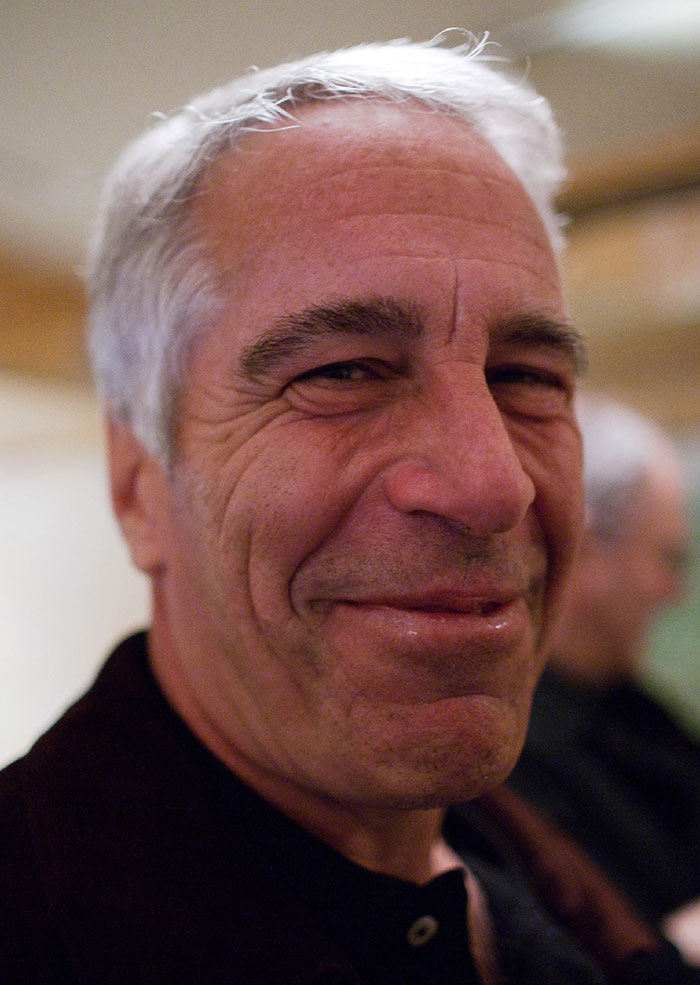 Close-up of a man with gray hair smiling softly in an indoor setting, related to Epstein files and photos of women.