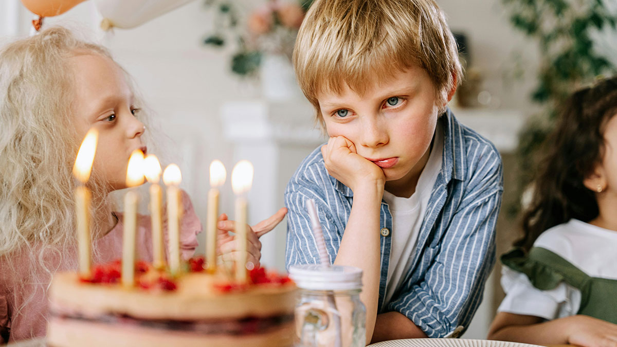 Sad boy at birthday party with cake and candles, reflecting a Jehovah's Witness mom's celebration under new name.