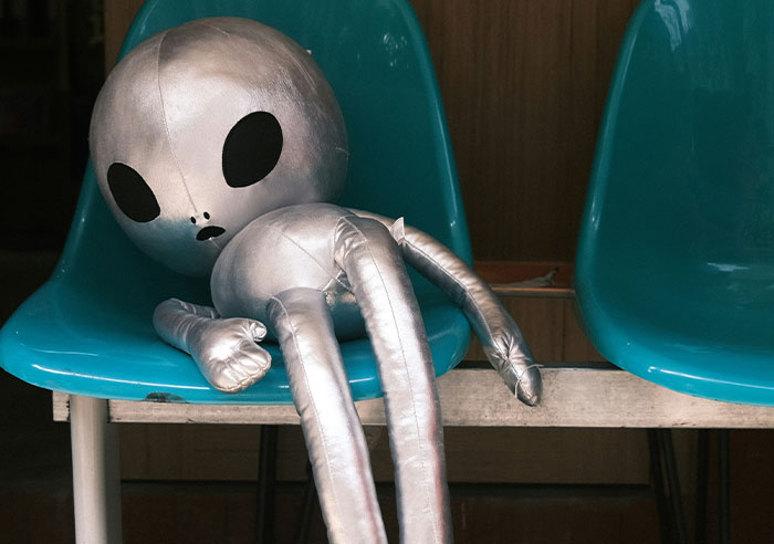 Silver alien doll slumped on a blue chair, illustrating mental questions job candidates decided to ask recruiters.