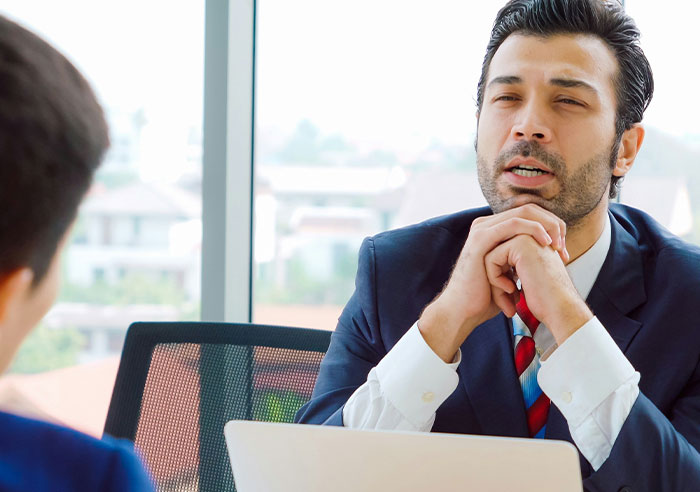 Two professionals in a job interview, with one candidate asking mental questions to the recruiter in an office setting.
