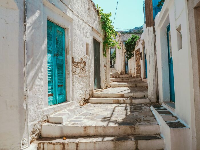 Narrow stone street in a Greek village with whitewashed buildings and blue doors under bright sunlight. Narrow stone street in a Greek village with whitewashed buildings and blue doors under bright sunlight.