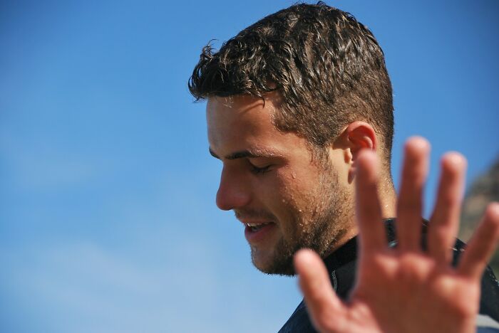 Young man with wet hair and beard outdoors raising his hand, illustrating harmless but toxic habits awareness.