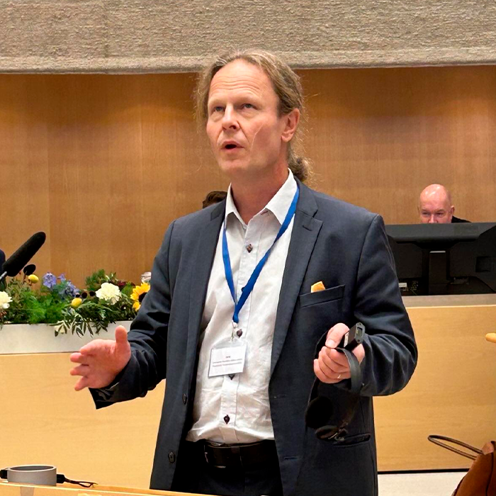 Man in a suit speaking at a podium during a formal session on Japan government and Finland beauty queen controversy.