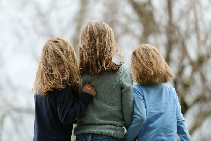 Three children standing together outdoors with backs turned, evoking feelings of trust and hidden dark secrets.