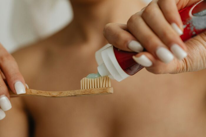 Close-up of hands applying toothpaste to a toothbrush, illustrating common everyday things people accidentally did wrong.