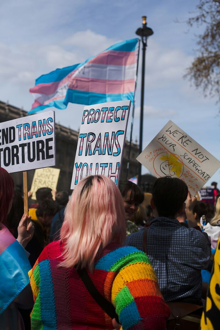 Manifestantes segurando cartazes defendendo os direitos dos jovens trans com uma bandeira do orgulho transgênero tremulando ao fundo. Manifestantes segurando cartazes defendendo os direitos dos jovens trans com uma bandeira do orgulho transgênero tremulando ao fundo.