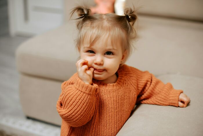 Toddler with pigtails wearing an orange sweater sitting on a couch representing bizarre and unbelievable baby names.