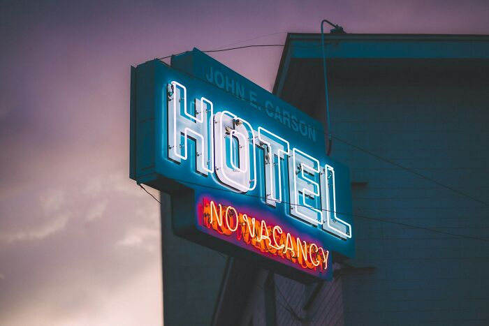 Neon hotel sign glowing at dusk with a no vacancy message, evoking stories of backstabbing and regret.