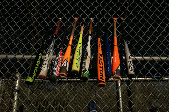 Various colorful baseball bats hanging on a chain-link fence, part of lost things owners never returned for.