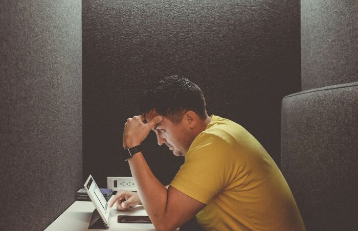 Man in yellow shirt working intensely on tablet in dim room illustrating digital nomad lifestyle challenges unseen on Instagram