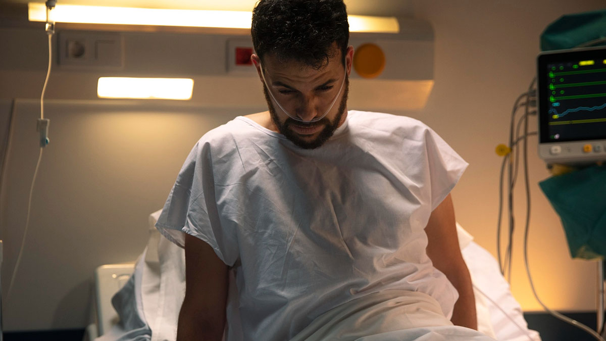 Patient with nasal oxygen tube sitting on hospital bed looking down during nighttime hospital stay