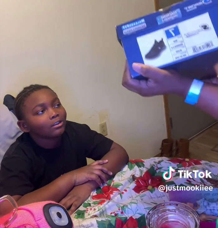 Boy sitting at a table with Christmas decorations, reacting to Angel Tree gifts being shown by an adult hand. Boy sitting at a table with Christmas decorations, reacting to Angel Tree gifts being shown by an adult hand.