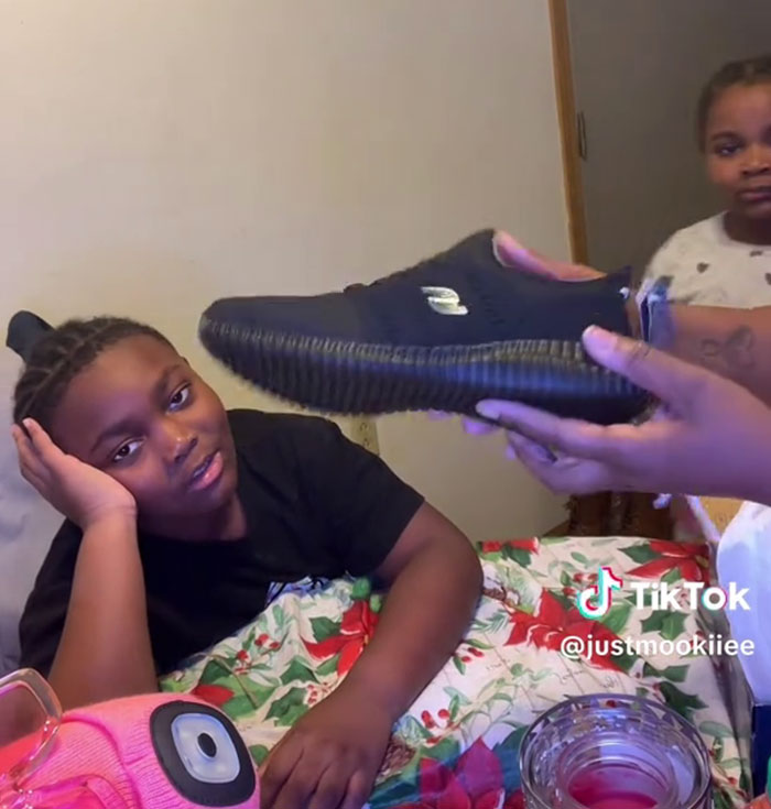 Boy showing ungrateful reaction to Angel Tree gifts as a woman holds out a shoe during a filmed family moment on TikTok.