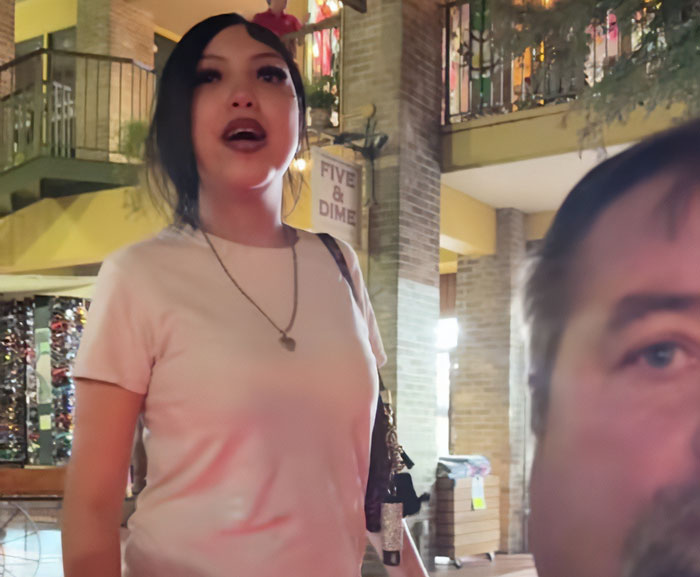 Teen in a pink shirt standing indoors near a brick pillar, related to judge teaching harsh lesson after pepper-spraying tourists on boat.