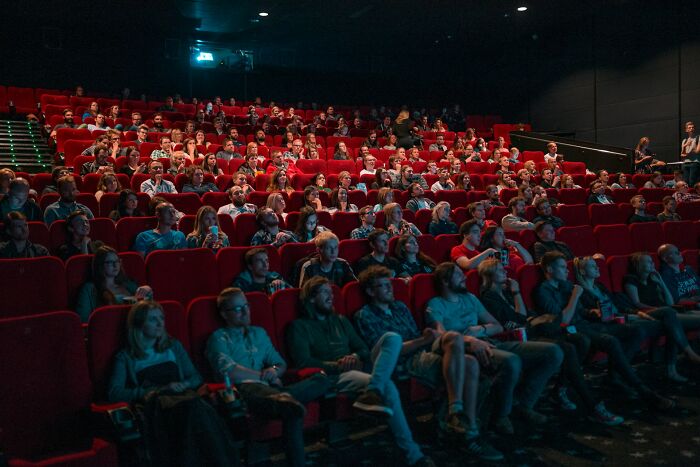 Audience seated in a dark theater watching a presentation about glitches in the system and how people exploited them.