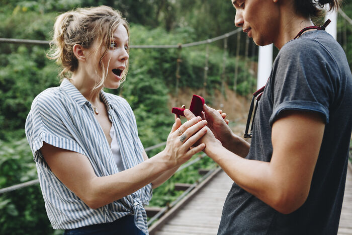 Young woman reacting with surprise as man presents a small red box outdoors, depicting a moment like a painful friendship breakup.