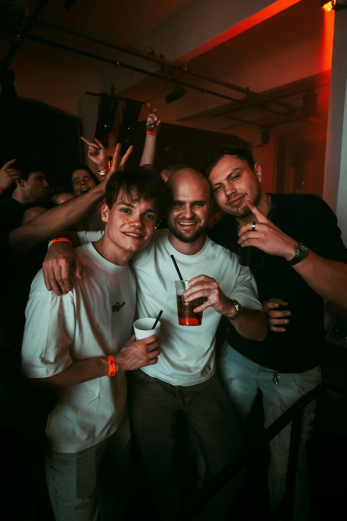 Three young men smiling and holding drinks at a party, capturing a moment of instant karma with friends enjoying the night.