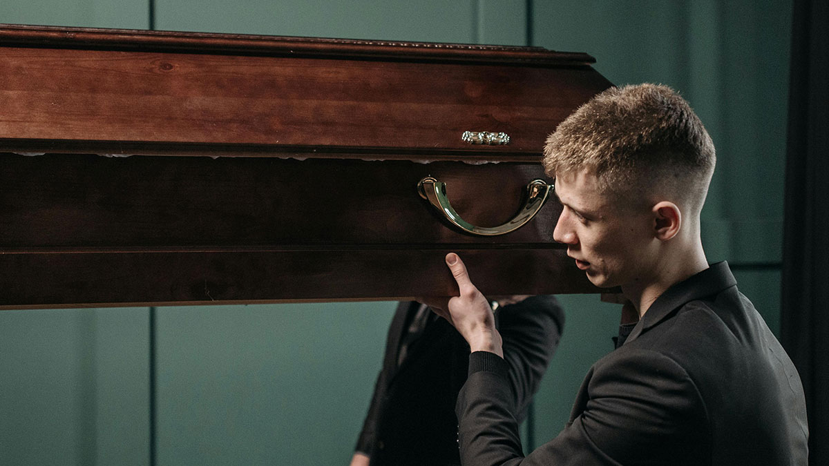 Young man in luxury industry carrying an expensive wooden coffin highlighting things the rich pay for rip-offs