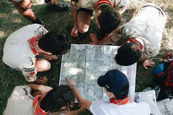 Group of scouts in uniforms gathered outdoors, examining a large map during an outdoor navigation activity.
