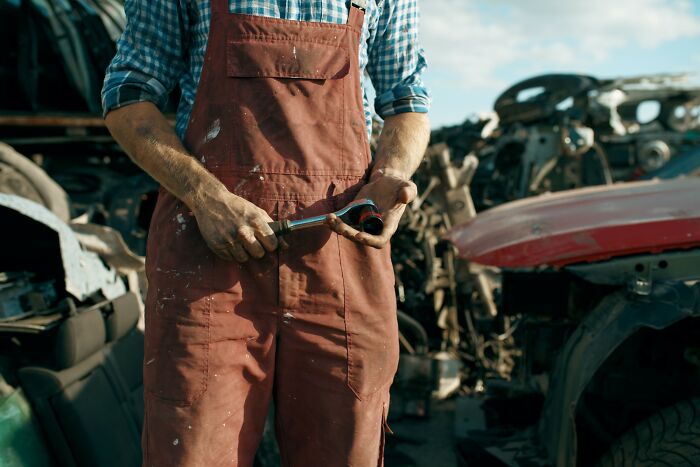 Mechanic in red overalls working with a wrench in an automotive scrapyard, representing genius without a degree.