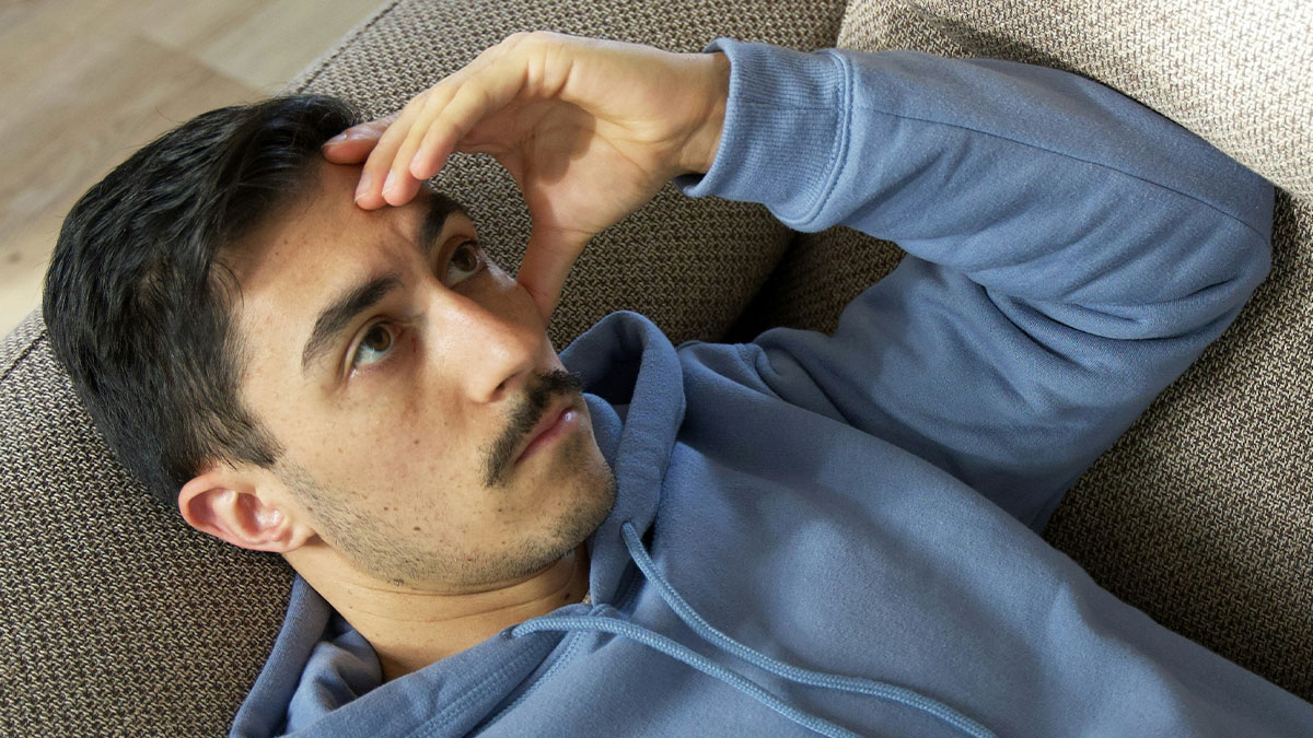 Man in blue hoodie lying on couch, looking confused while thinking about how he eats baked potato his way