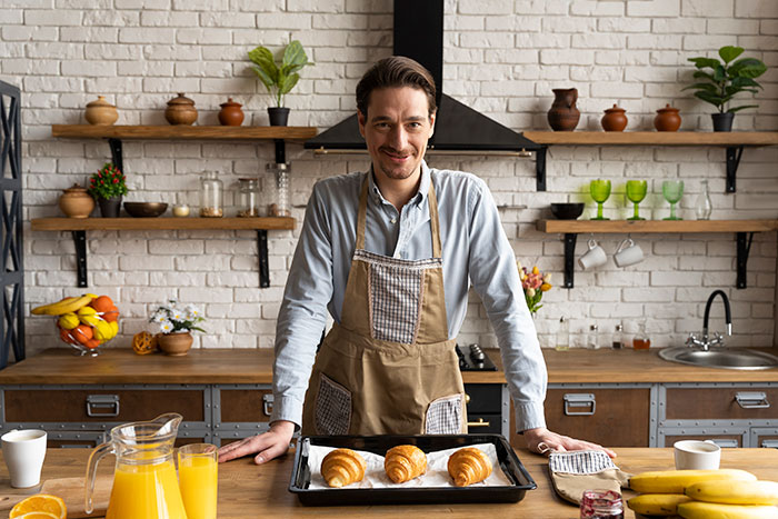 Man in apron presenting freshly baked pastries on tray in a kitchen, highlighting boyfriend's passion for pastries. Man in apron presenting freshly baked pastries on tray in a kitchen, highlighting boyfriend's passion for pastries.
