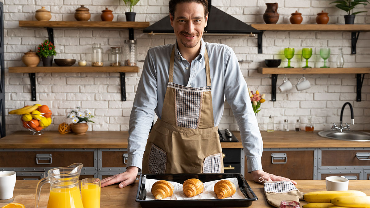 Man wearing apron in kitchen with freshly baked pastries, showcasing boyfriend's passion for pastries and baking.