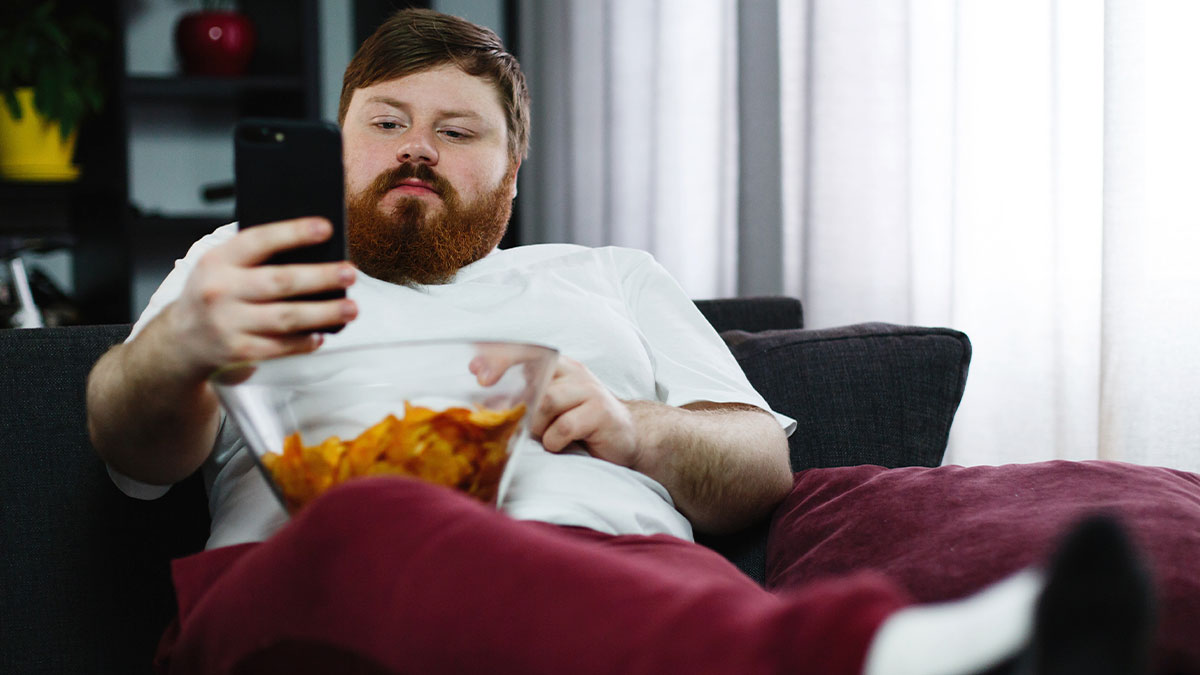 Man venting online about girlfriend wanting him to close her closet door, sitting on couch with snacks and phone.