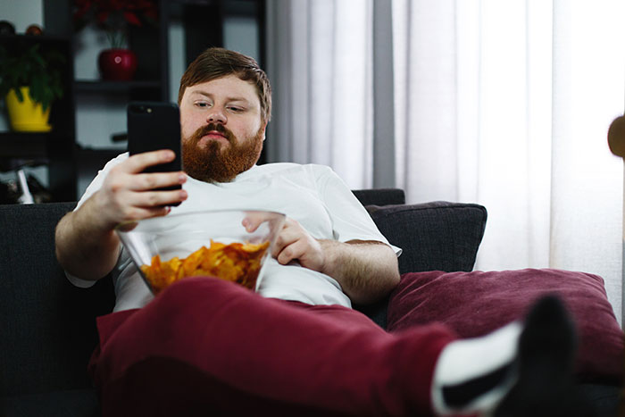 Man in casual clothes lounging with a bowl of chips, scrolling on his phone, representing guy vents online and girlfriend claps back. Man in casual clothes lounging with a bowl of chips, scrolling on his phone, representing guy vents online and girlfriend claps back.