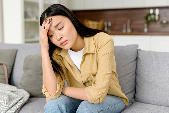 Young woman sitting on a couch looking worried and stressed, contemplating canceling wedding after family hires a PI Young woman sitting on a couch looking worried and stressed, contemplating canceling wedding after family hires a PI